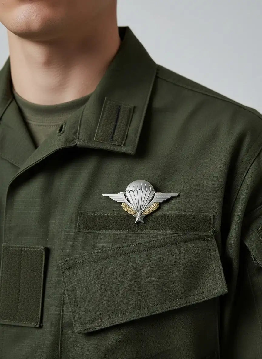 Insigne d’ailes de parachute argenté avec couronne de laurier dorée et étoile, fixé sur un uniforme militaire vert olive.